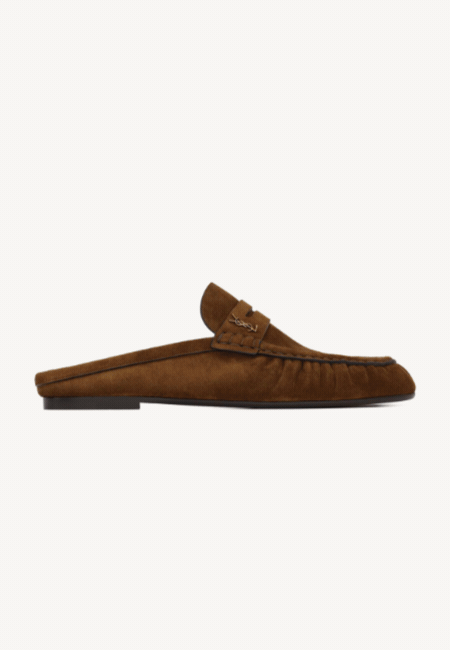 Kahverengi süet dokulu, arkası açık tasarımıyla zahmetsiz şıklık sunan, üzerinde belirgin dikiş detayları ve ön kısmında minimal YSL logosu bulunan bu loafer terlik, 2026 İlkbahar-Yaz moda trendlerinin öne çıkan ve çok aranan parçalarından biri olarak sergileniyor.