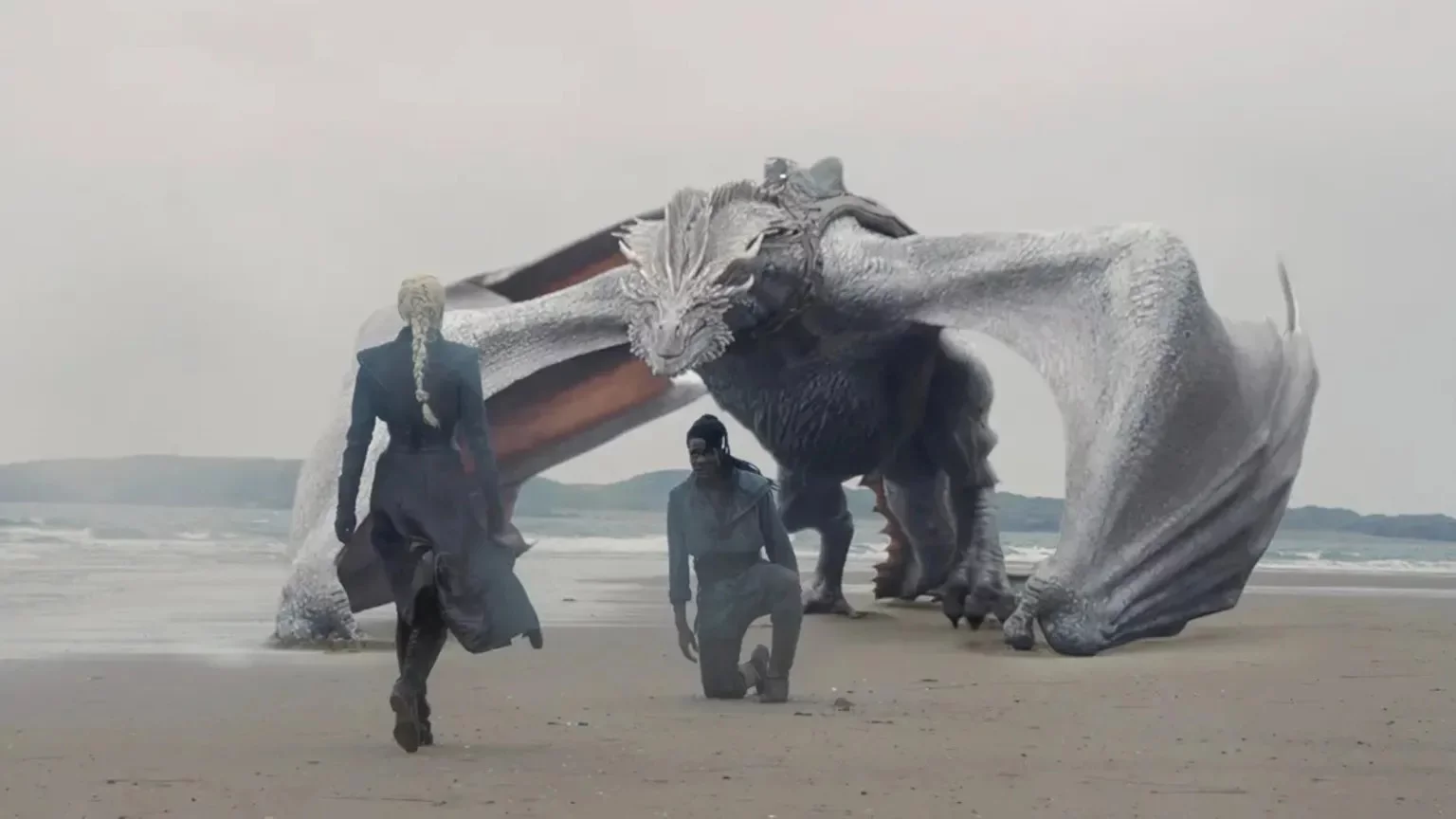 House of the Dragon dizisinden bir sahnede, kıyıda duran gümüş renkli devasa ejderha Seasmoke'un önünde Addam of Hull diz çökmüş; arkada Rhaenyra Targaryen ejderhadan uzaklaşarak kumlu sahilde yürüyor, bu an Ejderhaların Dansı'nda Siyahlar için kritik yeni bir ejderha binicisinin ortaya çıkışını simgeliyor.