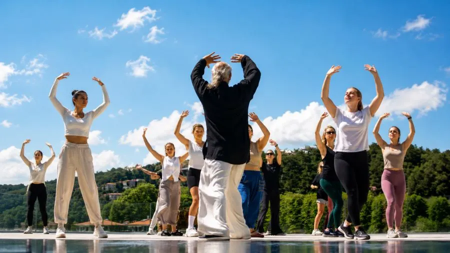 Güneşli bir günde, The Grand Tarabya'da Boğaz manzarası eşliğinde açık havada düzenlenen Tai Chi seansında, uzun saçlı eğitmen ve katılımcılar kollarını havaya kaldırarak sakin ve dengeli hareketler yapıyor.