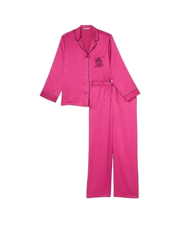 Beyaz bir zeminde sergilenen bu Victoria's Secret pijama takımı, fuşya rengi saten kumaştan yapılmış, üzerinde zarif monogram desenleri ve sol göğüs cebinde işlemeli bir logo barındıran uzun kollu gömlek ile uyumlu, beli lastikli ve geniş paçalı uzun bir pantolondan oluşmaktadır.