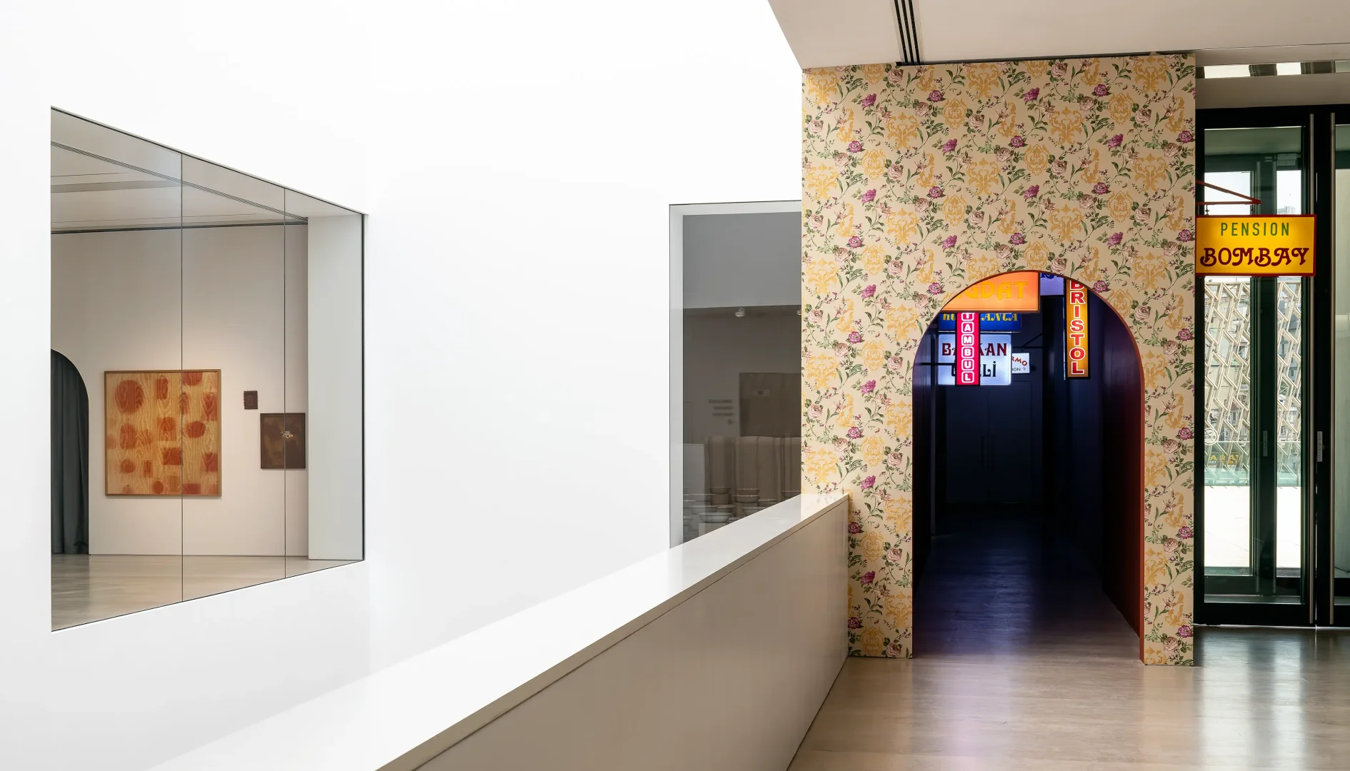 Beyaz duvarların ve aynada yansıyan ahşap dokulu soyut sanat eserlerinin modernliğini, çiçek desenli duvar kağıdıyla kaplı kemerli geçitten beliren neon PENSION BOMBAY ve BRISTOL tabelalarının eski Beyoğlu otel hafızasıyla harmanladığı bu iç mekan, semtin kültür rotasındaki tarihsel dönüşümleri vurguluyor.