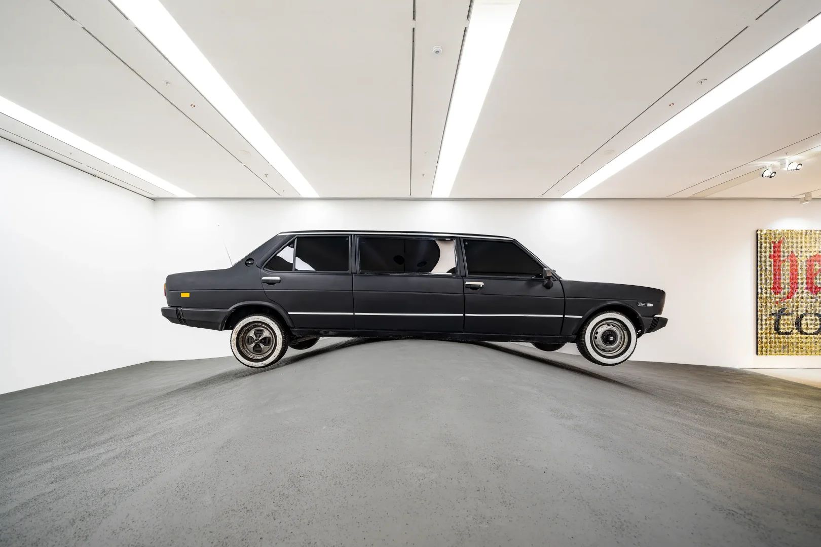 Modern ve beyaz duvarlı bir sanat galerisinde, gri dalgalı bir zemin üzerine yerleştirilmiş, mat siyah renkteki uzatılmış klasik bir otomobil heykeli, Beyoğlu kültür rotasının son durağı olan Arter'deki çağdaş sanat eserlerinden birini sergiliyor.