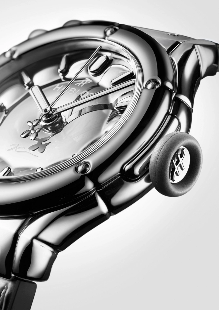 Gümüş rengi, parlak yüzeylere sahip Hublot Classic Fusion kol saatinin yakın çekiminde, Jeff Koons Balon Köpek temasını yansıtan üç loblu akrep ucu ve lastik biçimli kurma kolu detaylarıyla özgün bir tasarım görülüyor.