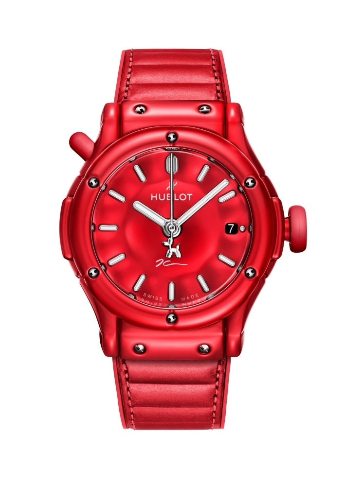 Parlak kırmızı Hublot Classic Fusion saati, kadranında sanatçı Jeff Koons'un imzasını ve ikonik balon köpek figürünü taşıyan, gümüş renkli indeksleri, ibreleri ve tarih göstergesiyle dikkat çeken lüks ve sanatsal bir tasarımdır.
