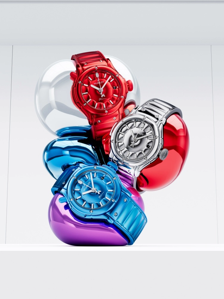 Beyaz bir zeminde, Jeff Koons iş birliğiyle üretilen kırmızı, parlak gümüş ve canlı mavi renklerdeki üç Hublot Classic Fusion kol saati, Koons'un ikonik balon köpek heykellerinden ilham alan, aynı tonlarda yansıtıcı balon formlarının üzerinde sergileniyor.