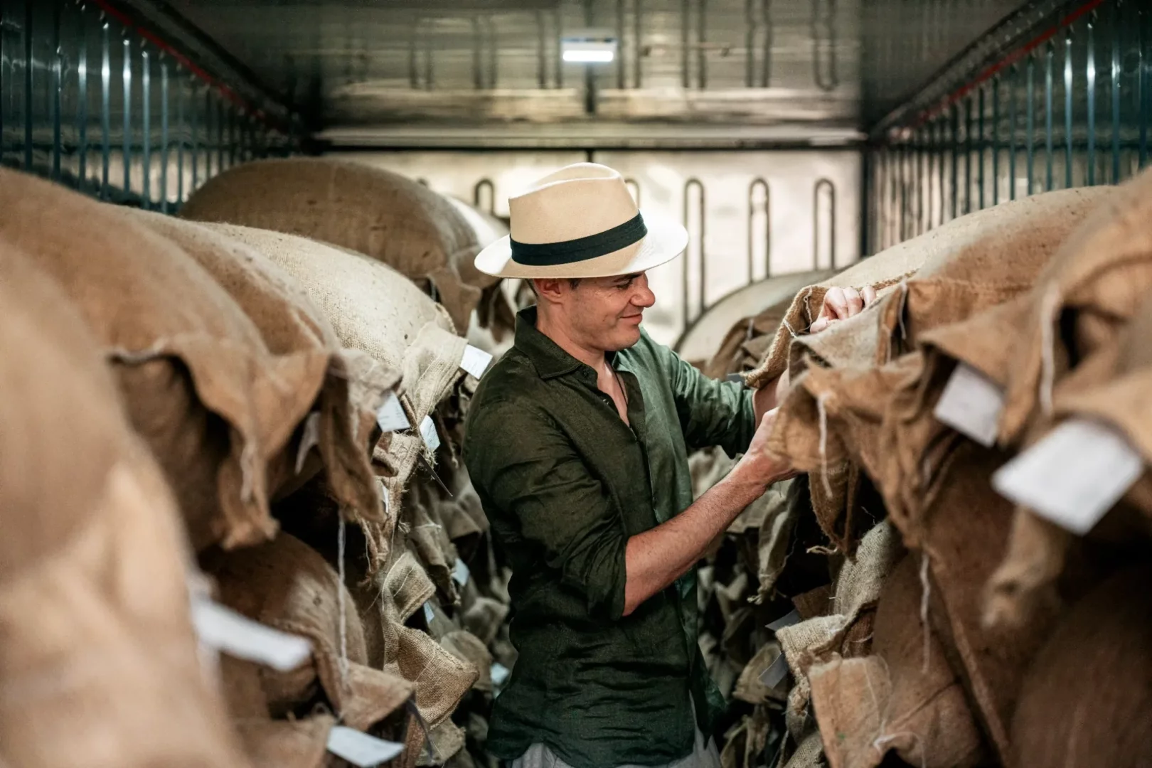 Metal duvarlarla çevrili bir depoda, şapkalı bir adam, iyi çikolatanın temelini oluşturan kaliteli kakao çekirdeklerinin özenle seçilmesini ve korunmasını temsil eden, yığınlar halindeki kaba dokulu jüt çuvallardan birini dikkatle inceliyor.
