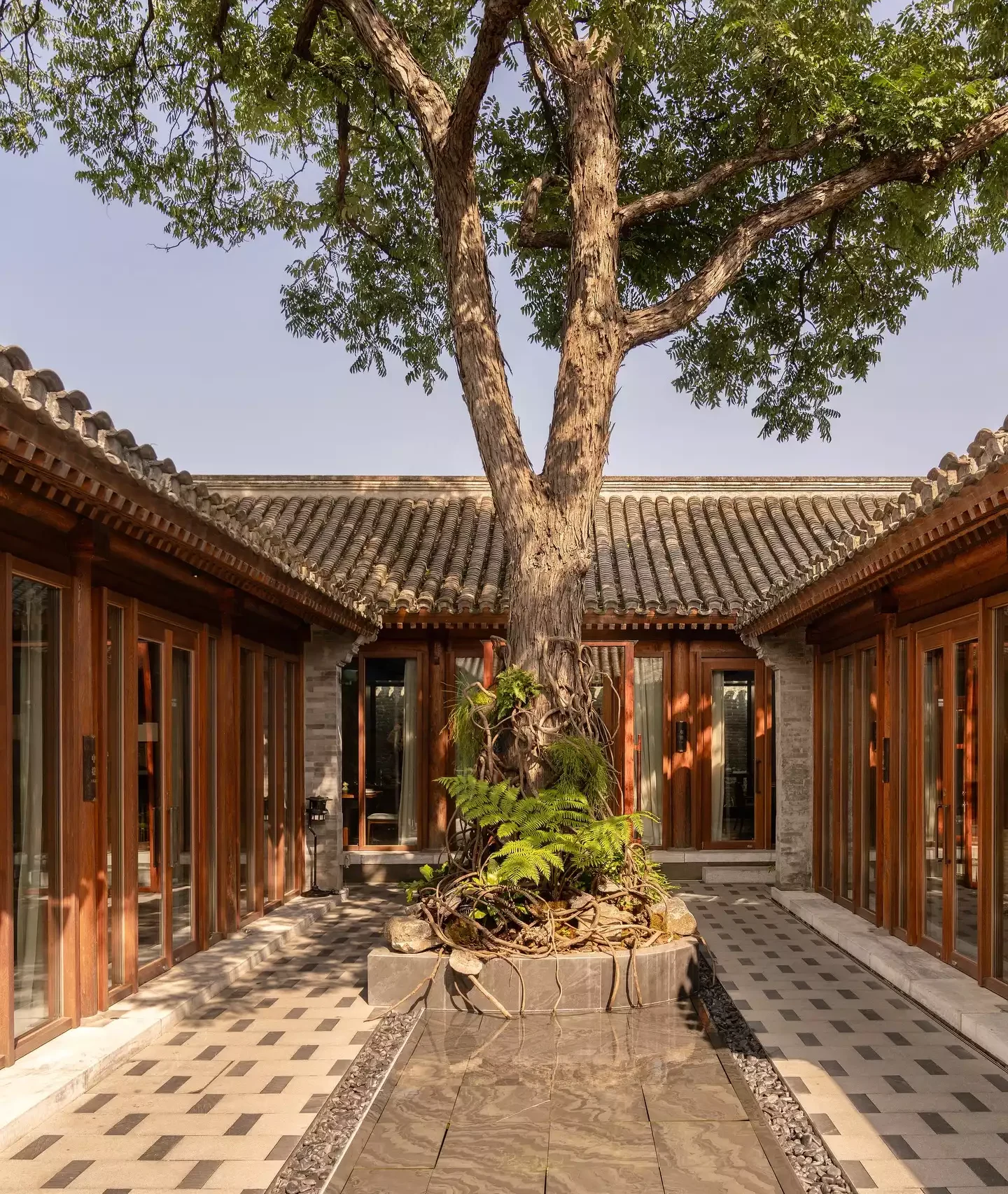 Mandarin Oriental Qianmen'deki geleneksel Çin avlusu, ortasında görkemli yapraklı dalları ve geniş kökleriyle büyük bir ağaç barındırıyor; çevresindeki klasik gri kiremitli çatılara sahip zarif ahşap çerçeveli cam kapılı binalar ve geometrik desenli döşemelerin yanı sıra yansıtıcı bir su ögesiyle huzurlu ve tarihi bir atmosfer sunuyor.