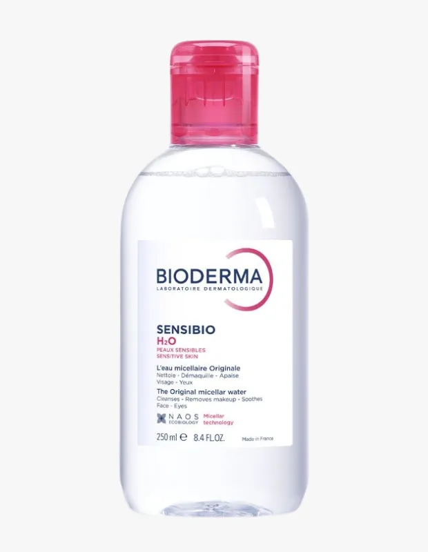 Beyaz etiketinde Bioderma Sensibio H2O ibaresi ve hassas ciltler için olduğu belirtilen, parlak pembe kapaklı, şeffaf, 250 ml'lik bir misel su şişesi temiz beyaz bir zemin üzerinde dikey olarak gözüküyor.