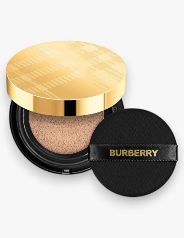 Parlak altın rengi, ikonik Burberry ekose desenli kapaklı, içerisinde açık tonlu bir fondöten bulunan siyah bir cushion kutusu ve üzerinde altın rengi Burberry yazısı bulunan yuvarlak siyah aplikatör, bu Burberry Matte Glow Cushion fondötenin şık ve pratik tasarımını sergiliyor.