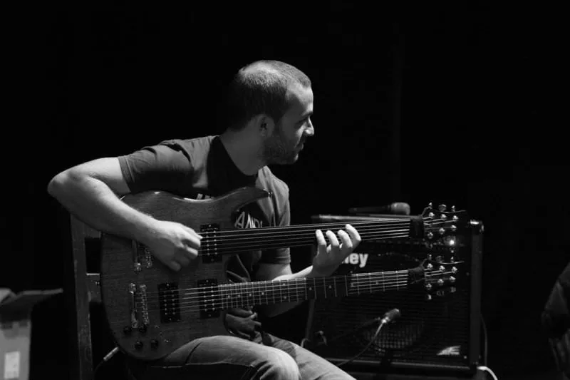 Cenk Erdoğan, Uluslararası İstanbul Gitar Günleri kapsamında sahnede çift saplı, biri perdesiz diğeri perdeli özel gitarıyla odaklanmış bir şekilde çalarken, gitar müziğine farklı bir yaklaşım sergiliyor.