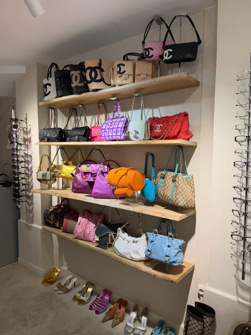 Duvarlara monte edilmiş ahşap raflarda sergilenen Chanel ve Gucci gibi lüks markalara ait, farklı renk ve modellerde onlarca tasarımcı çanta ile altında sıralanmış topuklu ayakkabılar ve yanda gözlük raflarının bulunduğu göz alıcı bir moda aksesuarları koleksiyonu.