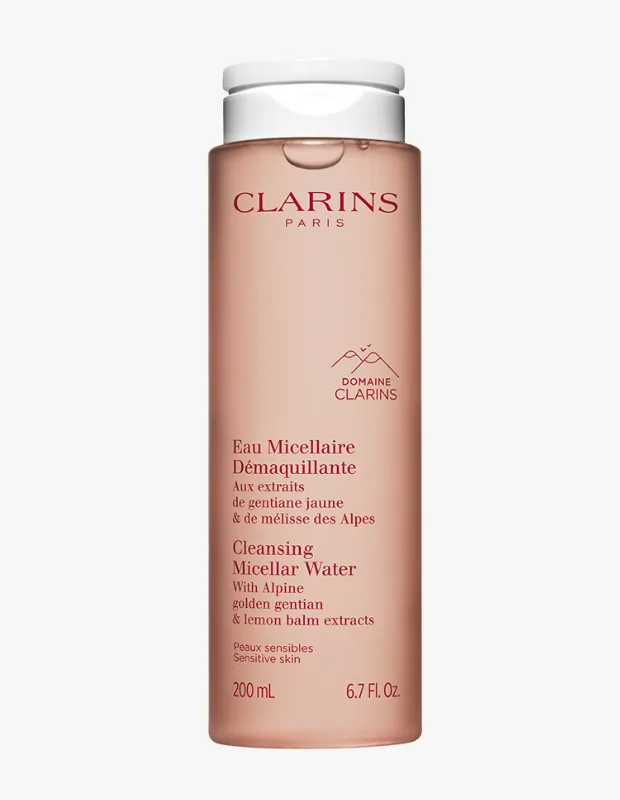 Aydınlık gri bir zeminde dik duran, yarı saydam şeftali pembesi renginde, beyaz kapaklı Clarins micellar su şişesi, üzerinde marka adı, 'Cleansing Micellar Water' ibaresi, 'Alpine golden gentian & lemon balm extracts' bilgisi ve hassas ciltler için olduğu notuyla birlikte 200 ml hacmini gösteriyor.