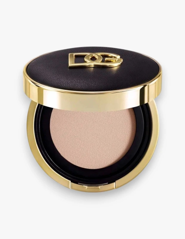 Parlak altın renkte D&G logosuyla süslenmiş siyah dokulu kapağı aralık duran, altın çerçeveli yuvarlak bir kutunun içinde görünen açık bej rengindeki bu Dolce & Gabbana Rose Glow yastık fondöten, aydınlatıcı ve nemlendirici etkisiyle SPF50 PA koruması sunuyor.