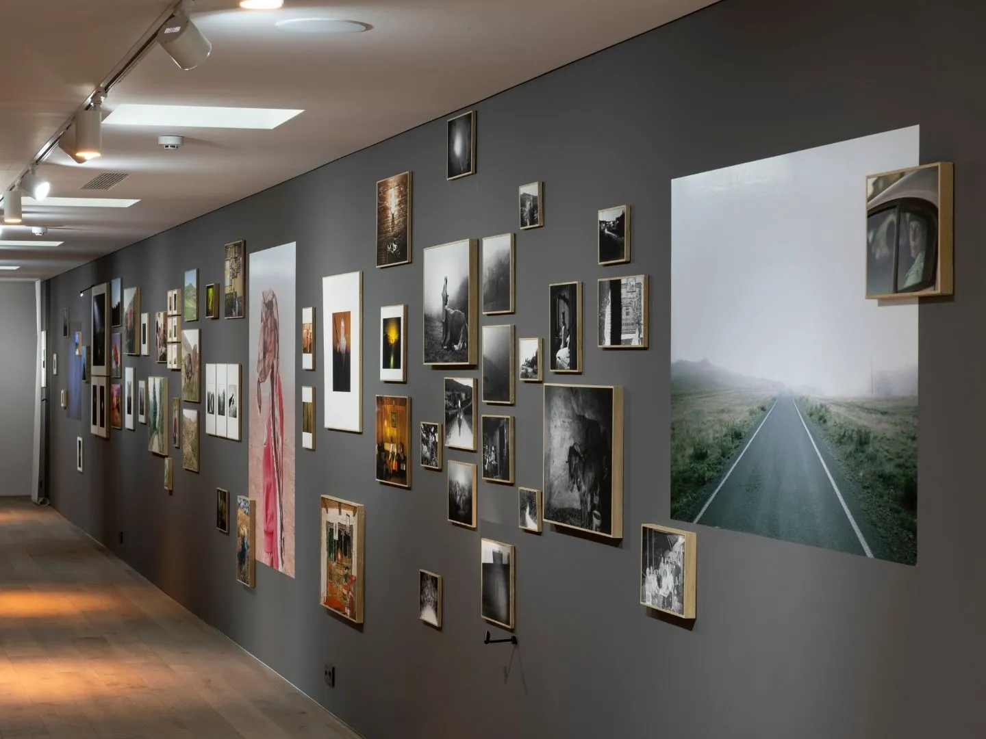 Hara İstanbul'daki bir sergide, gri duvarlara asılmış, farklı boyutlarda ve çerçevelenmiş sayısız fotoğraf eseri dikkat çekiyor; sisli bir yola uzanan büyük bir manzara fotoğrafı, çeşitli portreler ve şehir manzaralarıyla birlikte görsel bir şölen sunuyor.