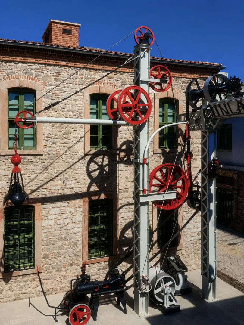 Taş bir binanın önünde, Güneşli bir günde, kırmızı tekerlekli, kasnaklı ve zincirli karmaşık gri metal bir endüstriyel makine düzeni, Koç Topluluğu’nun Yüzyılın İzleri sergisi kapsamında endüstriyel mirasın ve sanayi tarihinin nasıl korunup sergilendiğini gözler önüne seriyor.
