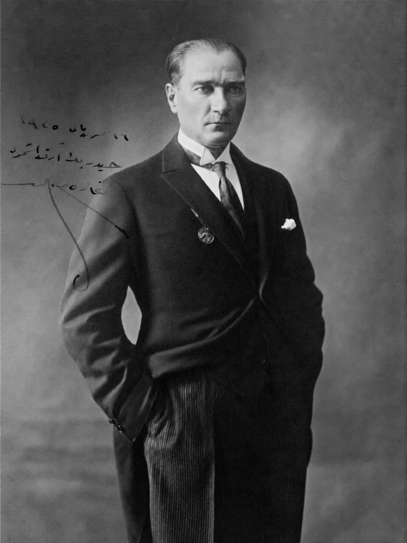 Siyah beyaz bir fotoğrafta, koyu renk takım elbisesi içinde elleri cebinde duran ve kararlı bakışlarla doğrudan izleyiciye yönelen Mustafa Kemal Atatürk portresi, Koç Topluluğu'nun Yüzyılın İzleri sergisinde Türkiye Cumhuriyeti'nin kuruluş ruhunu yansıtıyor.