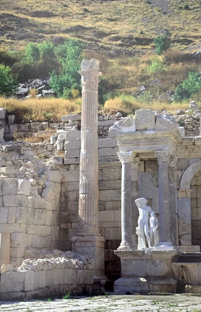 Sagalassos antik kentindeki Koç Topluluğu tarafından desteklenen arkeoloji çalışmalarının bir parçası olarak, güneşli bir günde, yivli uzun bir sütun ile başını kaldırmış çıplak bir erkek figürü ve yanındaki hayvan heykeline sahip, işlemeli mermer bir tapınak kalıntısının göründüğü bu yapı, Yüzyılın İzleri sergisinin geçmişle bugün arasındaki köprüsünü simgeliyor.