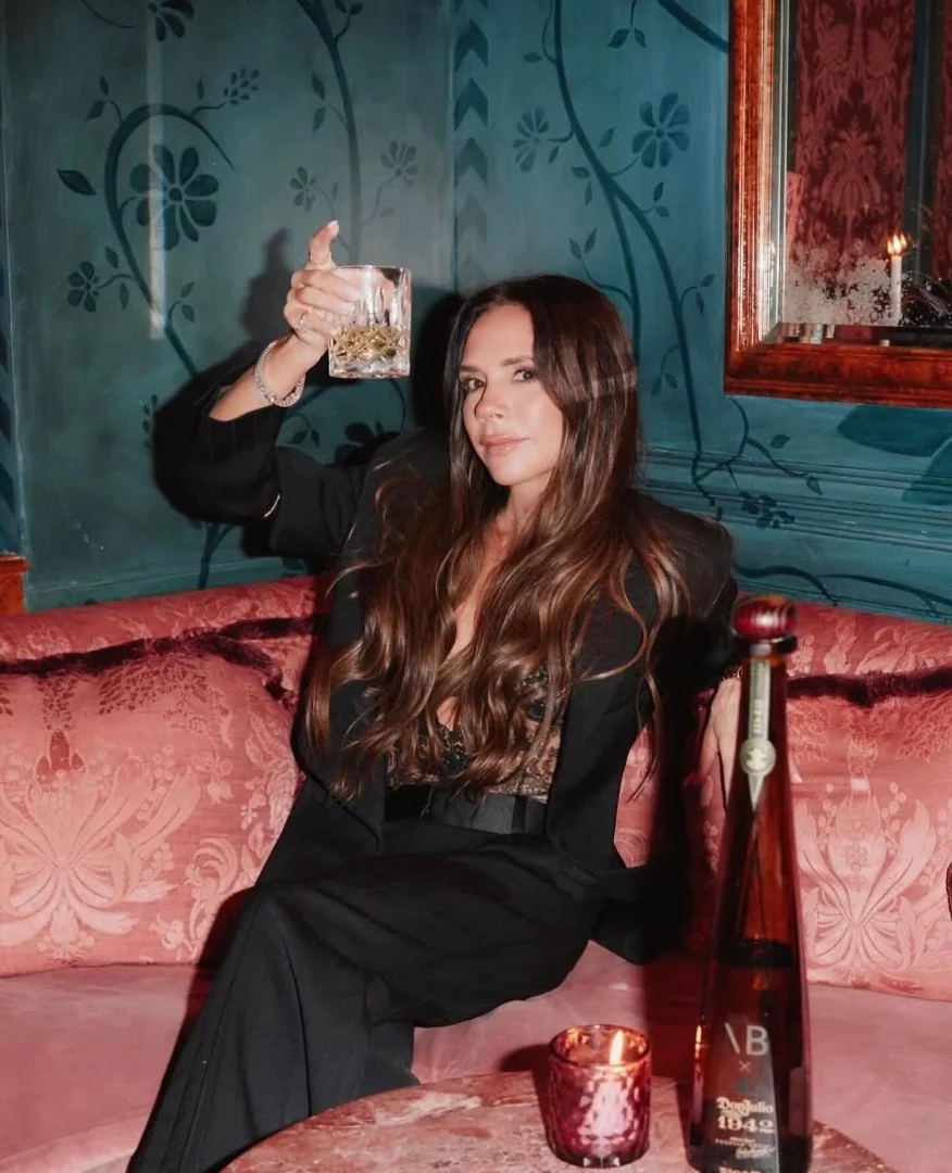 Lapérouse'un loş ışıklı, kadife kaplı, desenli duvarlara sahip özel salonlarından birinde, elinde buzlu bir içkiyle kameraya bakıp gülümseyen Victoria Beckham, masadaki yanan mum ve Don Julio 1942 şişesiyle Paris'teki romantik bir date gecesi atmosferini yansıtıyor.