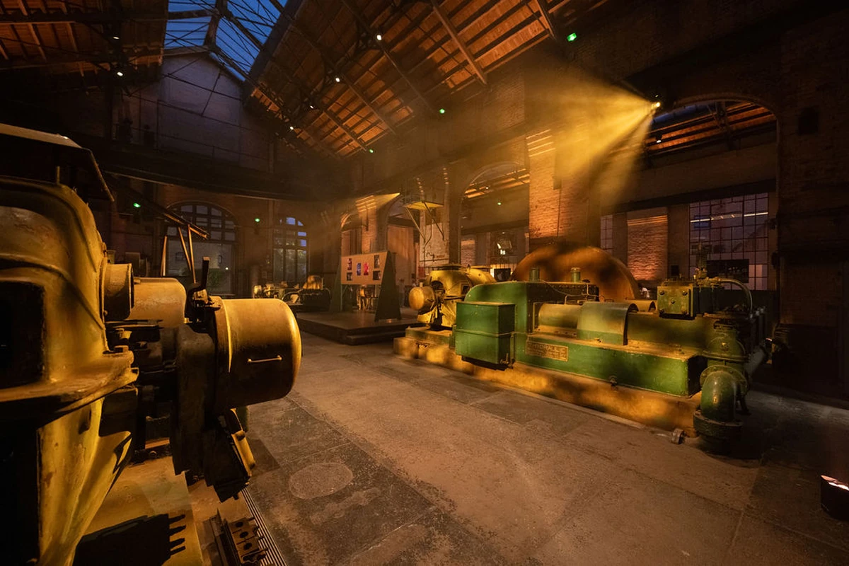 Wapping Hydraulic Power Station’ın yüksek tavanlı tarihi iç mekânında sarı ve yeşil tonlardaki eski hidrolik makineler, tavandan gelen spot ışıkları altında.