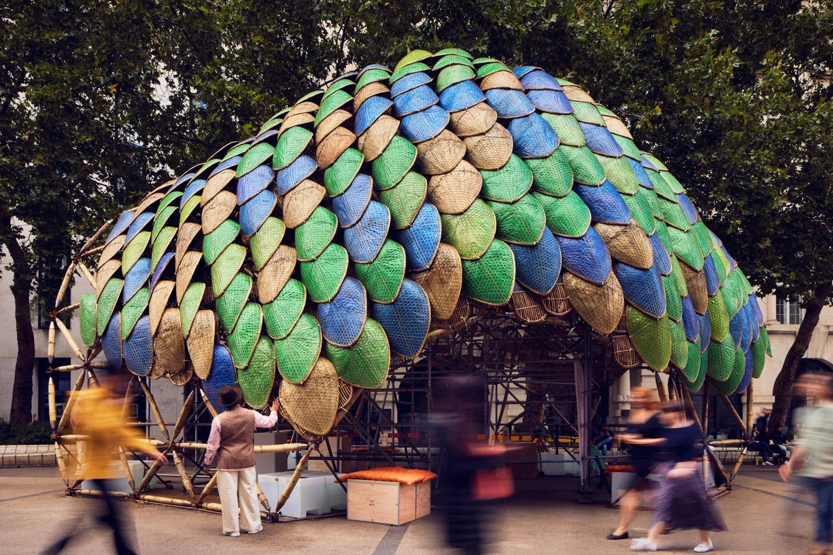 London Tasarım Festivali'nde sergilenen Studio Saar ve Atelier One'ın The Pangolin Shield enstalasyonu, bambu strüktür üzerine monte edilmiş yeşil, mavi ve doğal renklerdeki pullu panelleriyle dikkat çekerek, çevresindeki kalabalığı ağırlayan dev bir dış mekân yapısıdır.