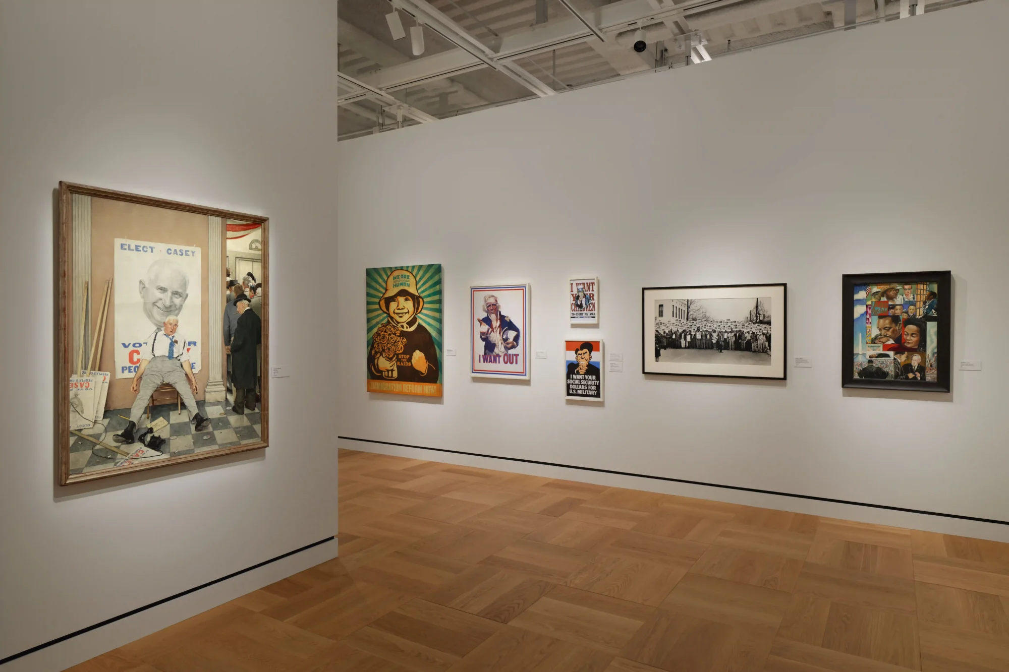 Lucas Museum of Narrative Art’ın bir galerisinde, solda Norman Rockwell’in seçmen posteri önünde yorgun bir adamı gösteren tablosuyla başlayan ve göçmenlik, savaş ile sivil haklar temalı posterler ve büyük bir topluluk fotoğrafının yer aldığı, görsel hikaye anlatıcılığını sergileyen çeşitli bir koleksiyon uzanıyor.