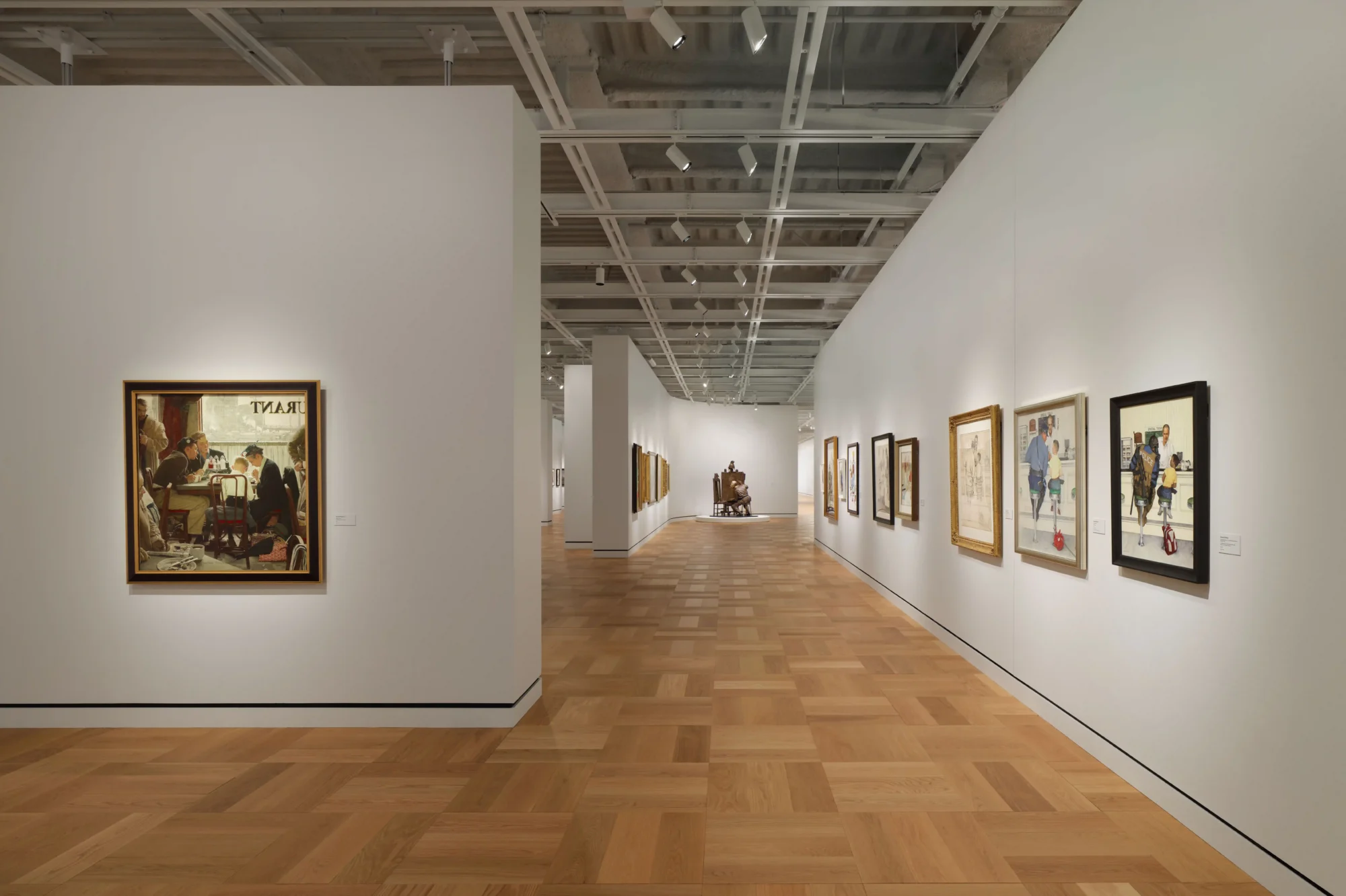 Beyaz duvarlı, açık renk ahşap parke zeminli, tavanından sarkan spot ışıklarıyla aydınlatılmış geniş bir sanat galerisinde, duvarlar boyunca sıralanmış farklı boyutlarda çerçeveli tablolar ve heykeller yer alıyor; bu görsel hikâye anlatıcılığı koleksiyonu, Lucas Anlatı Sanatı Müzesi'nin zenginliğini ve George Lucas'ın sanat dünyasına katkısını vurguluyor.