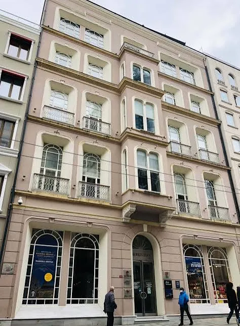 Bulutlu bir havada, önünde yürüyen insanların olduğu, açık pembe-bej renkli cephesiyle dikkat çeken çok katlı tarihi Merkez Han binası; demir parmaklıklı balkonları olan kemerli pencereleri, ortada yükselen cumba detayı ve giriş katındaki büyük kemerli dükkan vitrinleri ile şehrin dokusunu yansıtır.