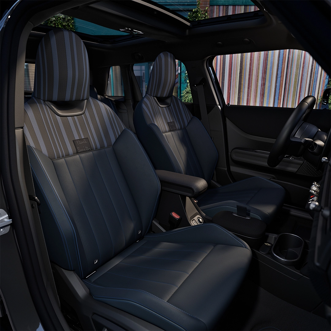 Mini Cooper Paul Smith Edition'ın dikkat çekici iç mekanında, dikey çizgili sırtlıklara ve Paul Smith yazısına sahip delikli koyu renkli koltuklar, ortada kol dayamalı konsol ve geniş açılır tavan göze çarparken, dışarıda renkli çizgili bir bina belirgin.