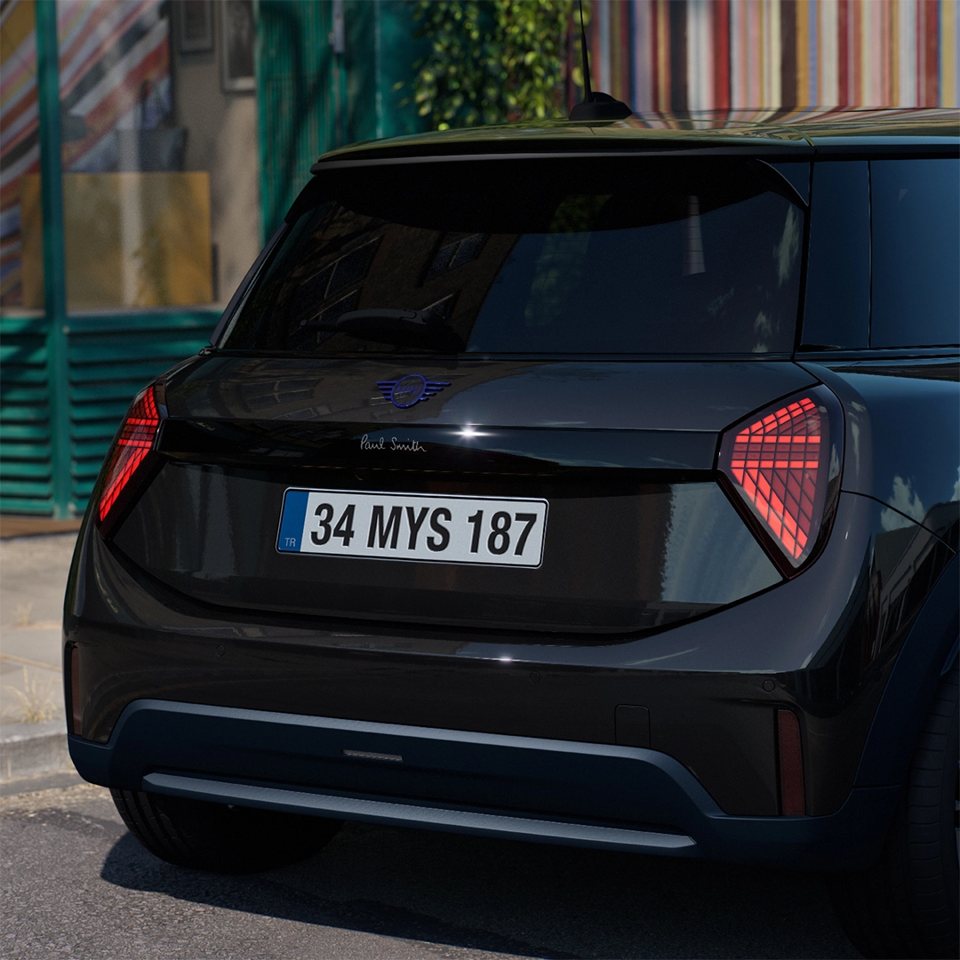 Arka planda binalar ve yeşilliklerin belirdiği şehir sokağında park edilmiş, Paul Smith Edition özel serisi siyah Mini Cooper otomobilin arka kısmının yakın çekiminde, Paul Smith logosu, belirgin kırmızı LED desenli üçgen arka lambaları ve 34 MYS 187 plakası net bir şekilde görülüyor.