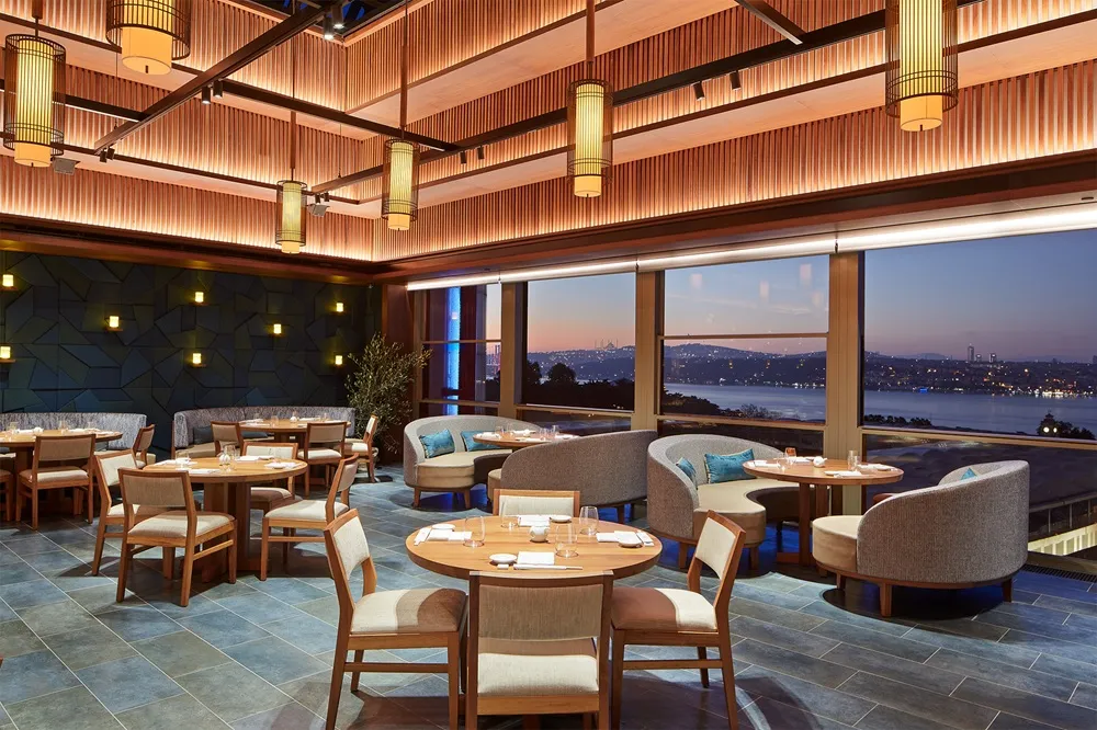 Nobu Istanbul'un Boğaz manzaralı zarif yemek salonu, sıcak ahşap detayları, şık masaları ve loş ışıklarıyla, Damien Duviau ve Michael De Jesus'un özel Four Hands Omakase ve cooking class programlarına ev sahipliği yapmaya hazır görünüyor.