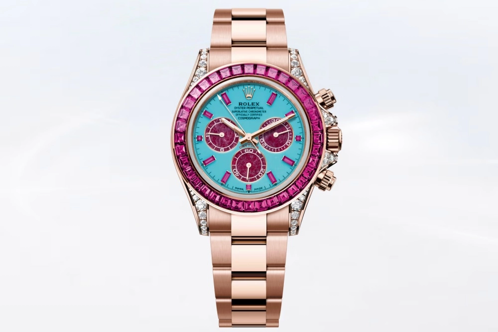 Pembe altın kasalı ve bilezikli, canlı turkuaz kadrana sahip, bezelinde ve saat göstergelerinde parlak yakut rengi dikdörtgen taşlar ile luglarında pırlanta detayları bulunan gösterişli bir Rolex Daytona saati.