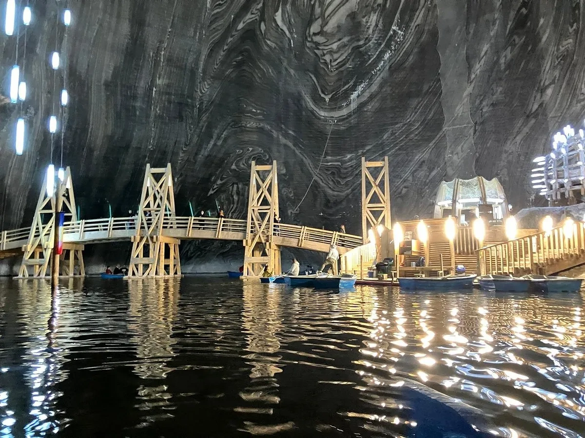 Romanya'daki Salina Turda tuz madeninin derinliklerinde, üzerinde ahşap bir köprü ve kiralık kayıklar bulunan yeraltı gölü, tavandan sarkan ve kıyılardaki ahşap iskeleleri aydınlatan ışıkların suya yansımasıyla büyüleyici bir atmosfer sunuyor.