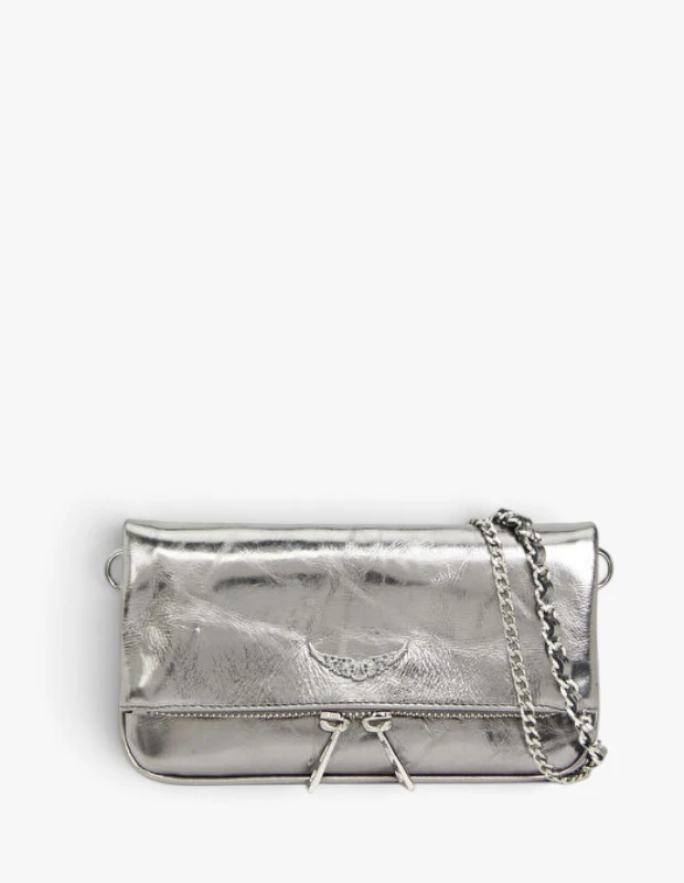 Parlak gümüş rengi, metalik dokulu deriden yapılmış, kapaklı tasarımı, kanat logosu ve önündeki çift fermuar detayıyla sonbahar-kış çanta trendlerini yansıtan zarif bir clutch çanta, kalın zincir askısıyla beyaz zeminde dikkat çekiyor.