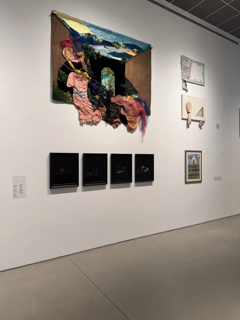 Beyaz bir galeride, tropikal bir sahne gösteren kemerli bir açıklığa sahip, farklı renklerdeki kumaşlarla bezeli üç boyutlu büyük bir tekstil sanatı eseri ve çevresindeki çeşitli çerçeveli yapıtlar, Koç Topluluğu'nun sanat koleksiyonundan